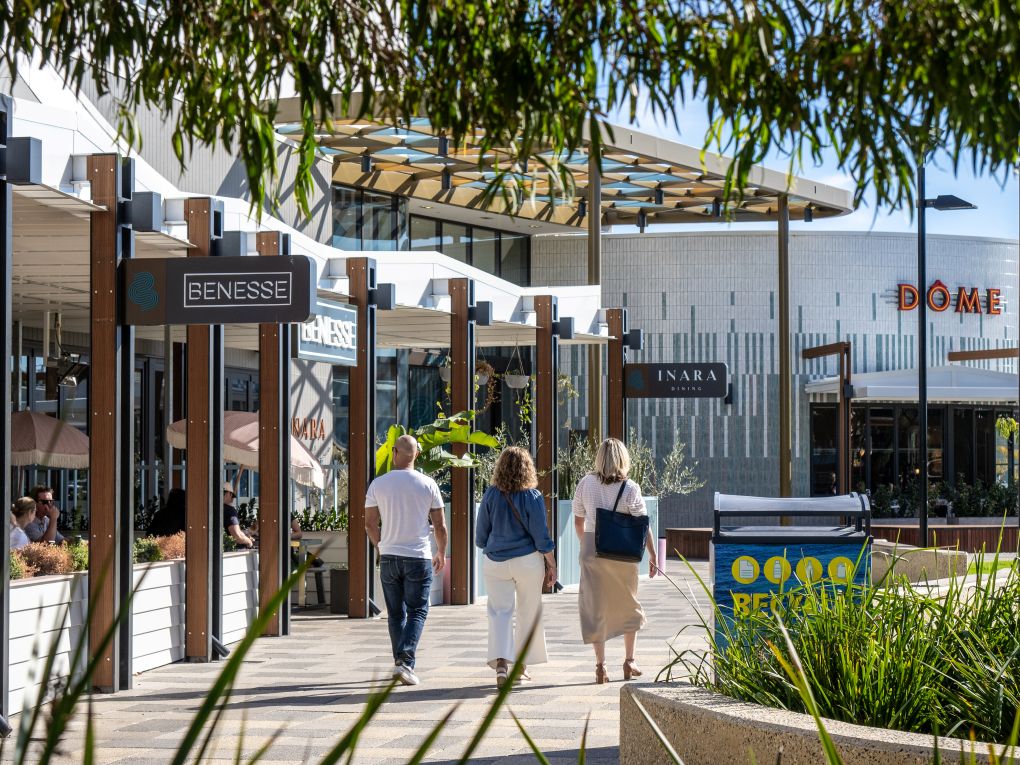 three people walking away from the camera, in front of a cafe with small green garden 