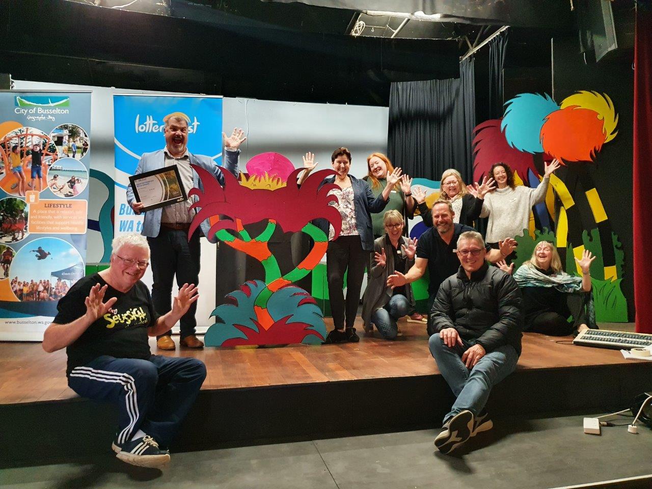 Group of people on a stage celebrating, surrounded by colourful props.